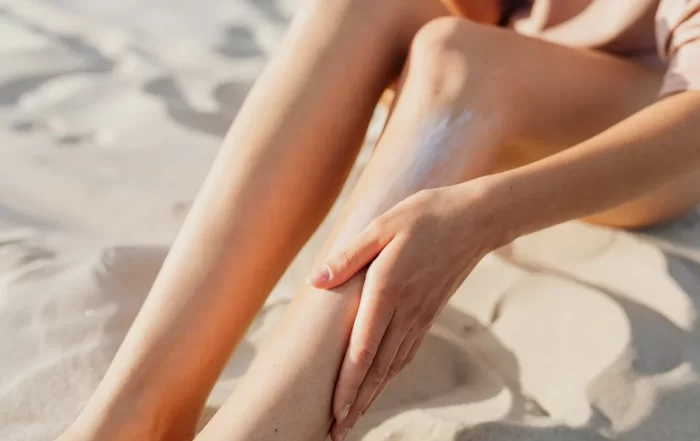woman on beach, applying sun screen to legs