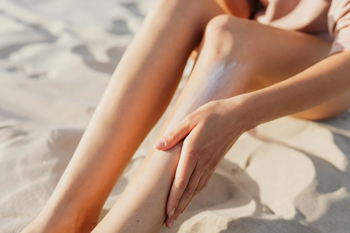 woman on beach, applying sun screen to legs